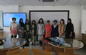 Participants of the BDOAA Women's Astronomy Olympiad Preparation Camp standing with an instructor in front of a whiteboard covered in blackbody and spectral energy distribution notes.
